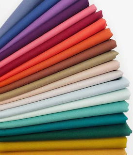 Stack of folded fabric swatches arranged in rainbow color gradient from cool to warm tones