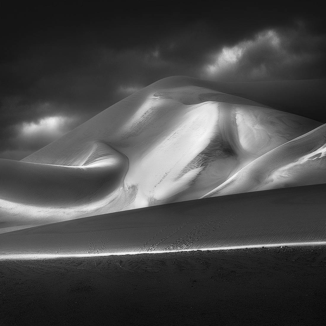 Black and white desert sand dunes beneath dark dramatic clouds