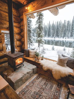 Cozy log cabin interior with wood stove and large window view of snowy pine forest and frozen lake