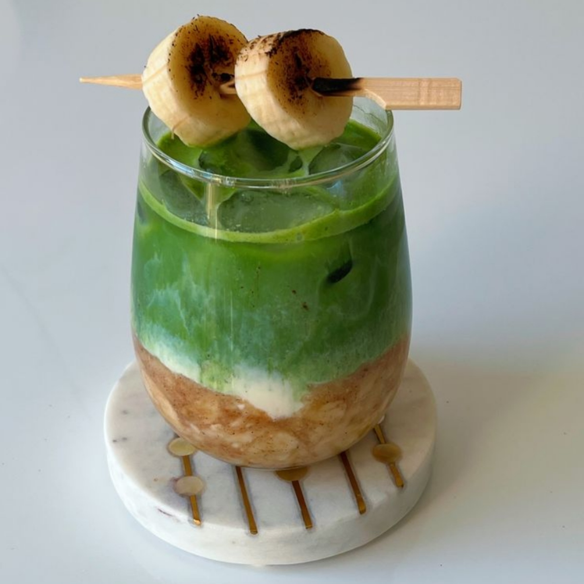 Layered matcha drink in a glass with banana slices on a skewer