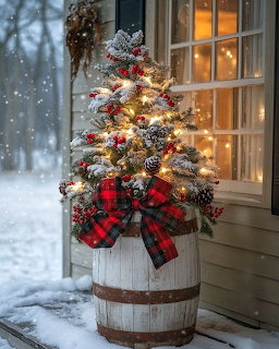 Lit miniature Christmas tree with red plaid bow in barrel on snowy porch at twilight