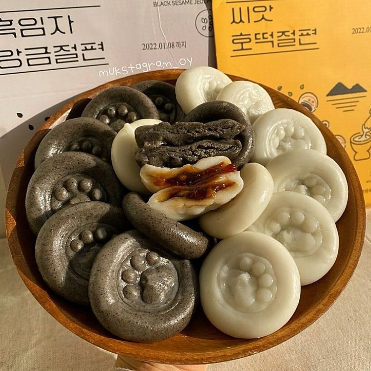Black and white Korean rice cakes with paw-print shapes arranged on a round wooden plate