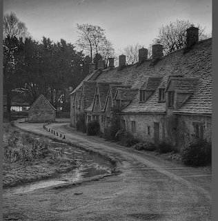 Black and white photo of historic stone cottages lining a rural road in the Cotswolds with bare winter trees