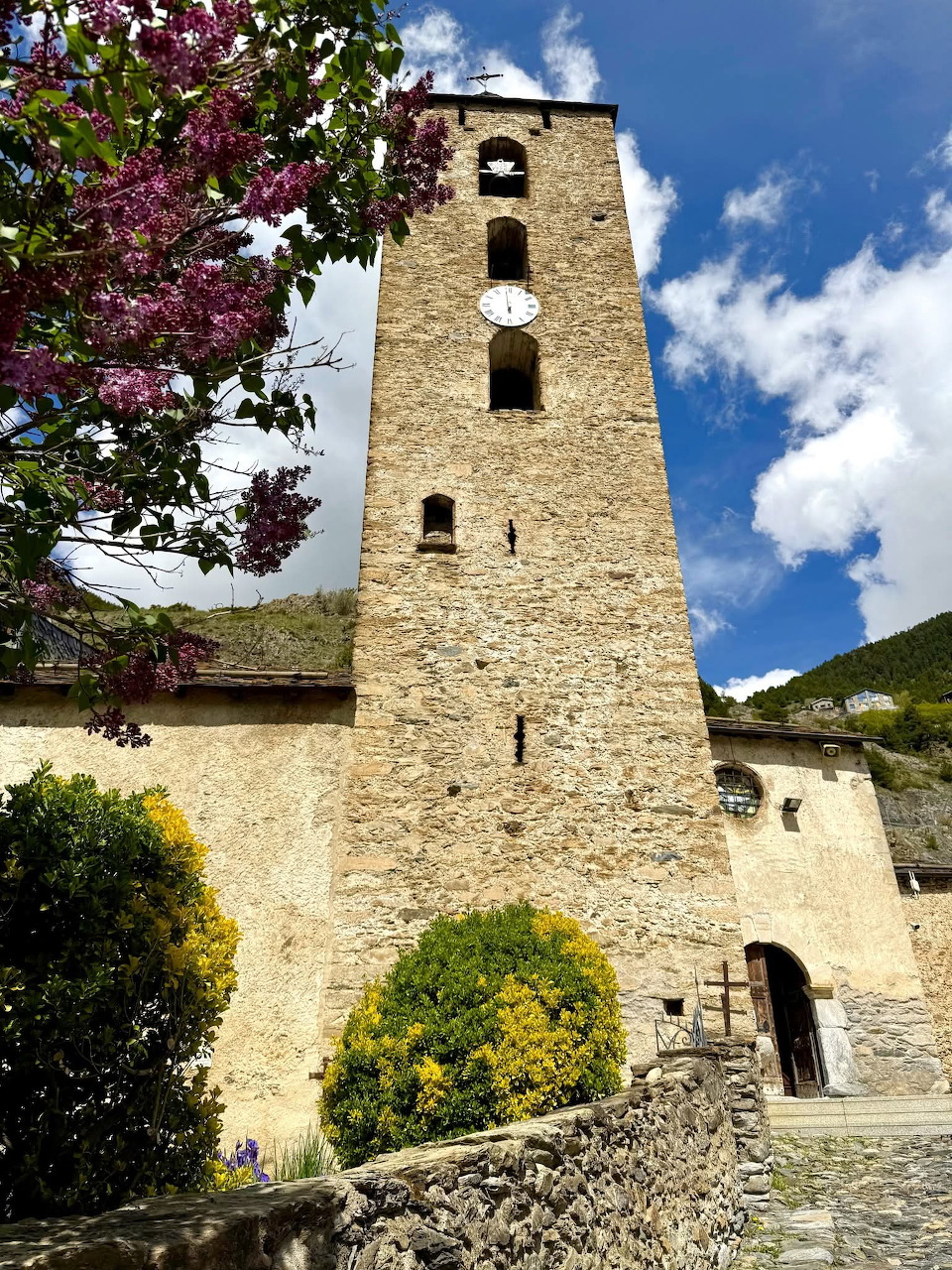 Tall stone church tower beside a cobbled path under a blue sky with clouds
