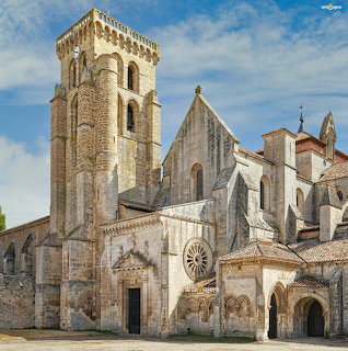 Old stone abbey with bell tower and arched entrances beneath a blue sky
