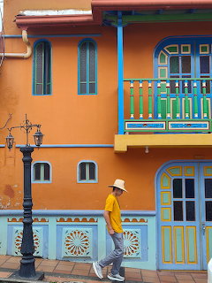 Man walking past a brightly painted orange and blue colonial building with decorative windows and balcony