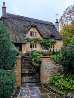 Stone cottage with thatched roof and iron gate entrance surrounded by garden