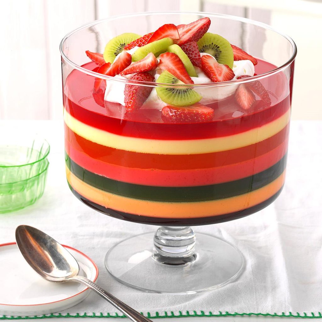 Seven-layer gelatin dessert with rainbow stripes topped with strawberries and kiwi in glass pedestal bowl