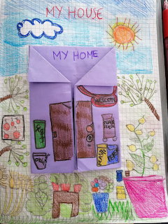Child's drawing of a house on graph paper with crayon sun, cloud, trees, flowers, and a paper fold envelope