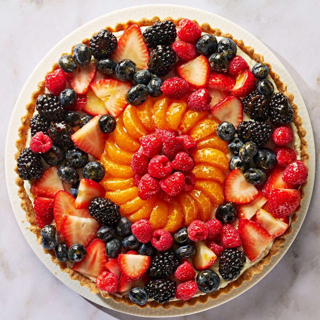 Circular fruit tart with berries and citrus arranged in colorful concentric rings on a white surface