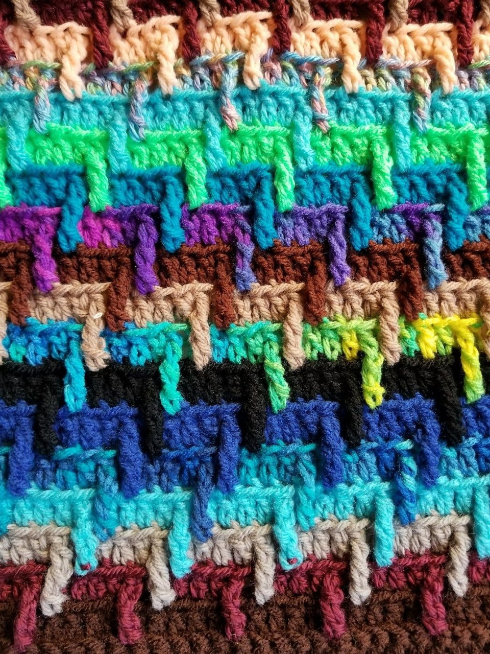 Close-up of a colorful knitted zigzag pattern with blue, green, purple, brown, and tan yarn