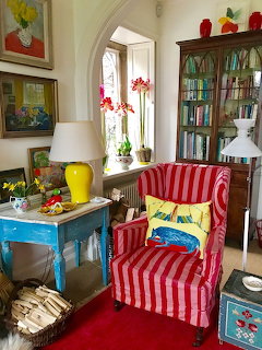 Red and white striped wingback armchair in a colorful room with paintings, bookcase, and blue table