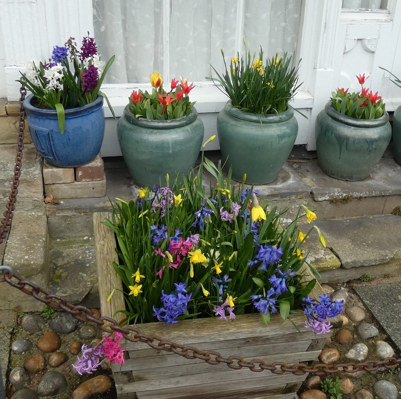 Colorful spring flowers in ceramic pots arranged on stone patio with wooden tray centerpiece