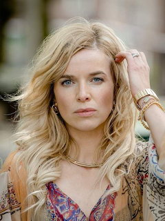 Blonde woman with wavy hair in a colorful patterned blouse posing outdoors