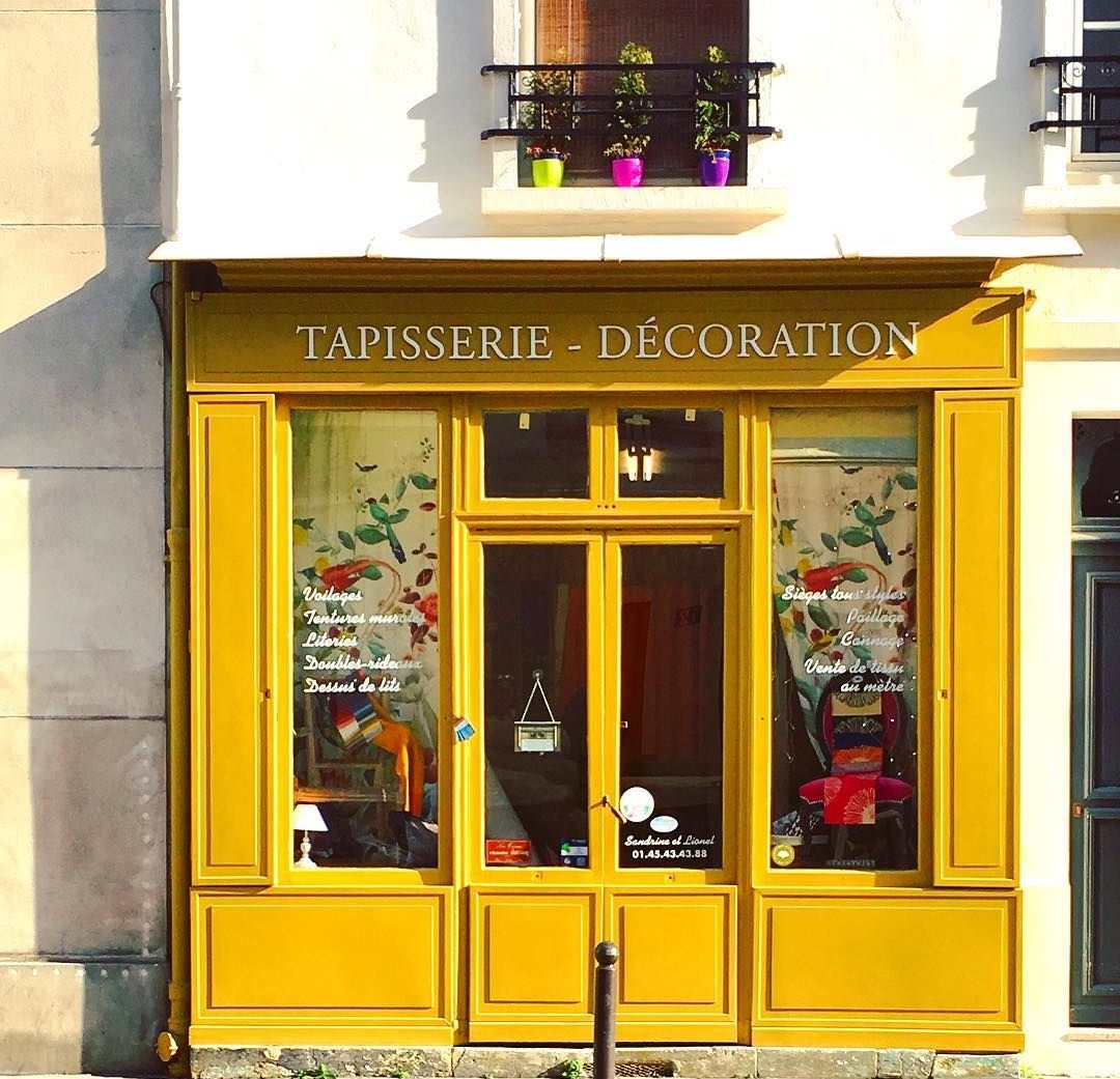 Yellow-painted tapisserie decoration shop facade with large display windows and floral decorations