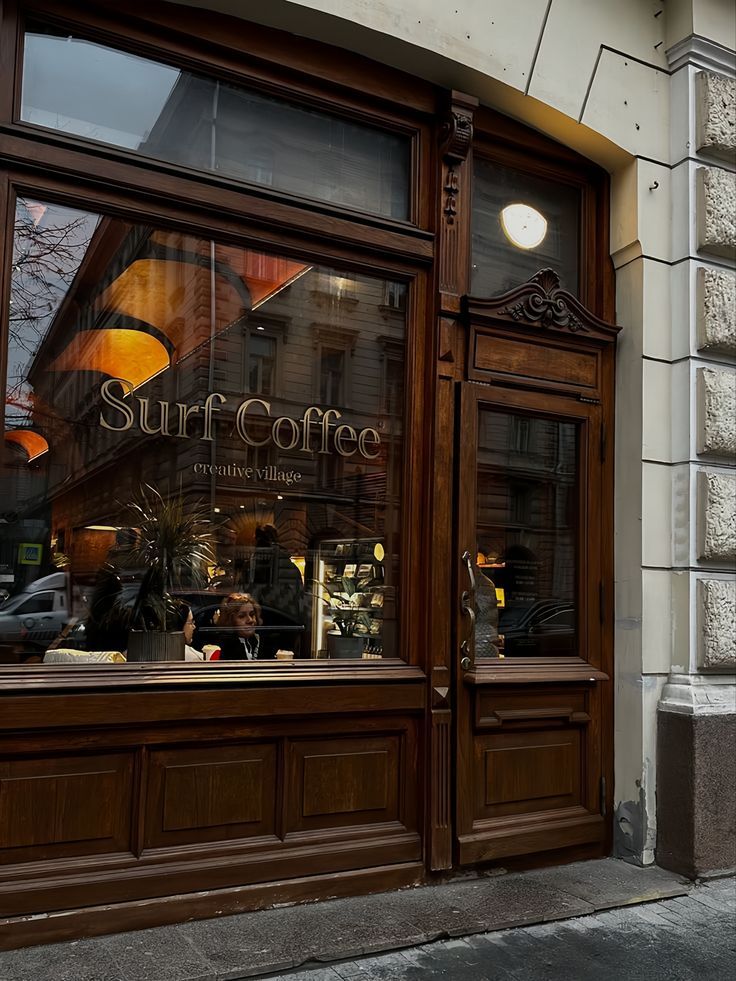 Dark wood coffee shop storefront with large windows and white columns at dusk