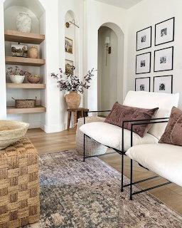 Bright living room with white sofa, brown pillows, patterned rug, arched doorways and wall art