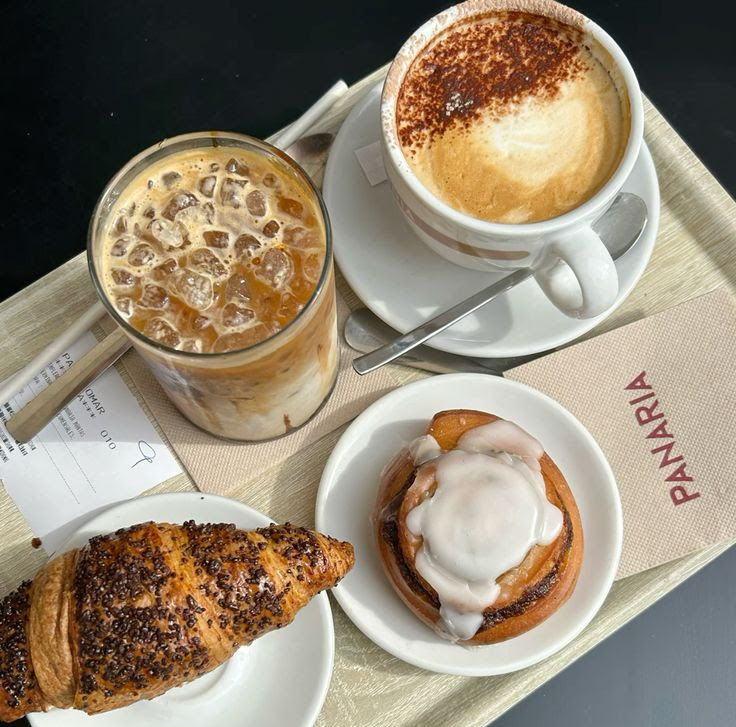 Top view of a tray with iced coffee, cappuccino, croissant, and iced cinnamon roll