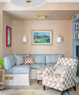 Cozy living room with blue patterned sofa, checkered chair, and framed landscape art on peach walls