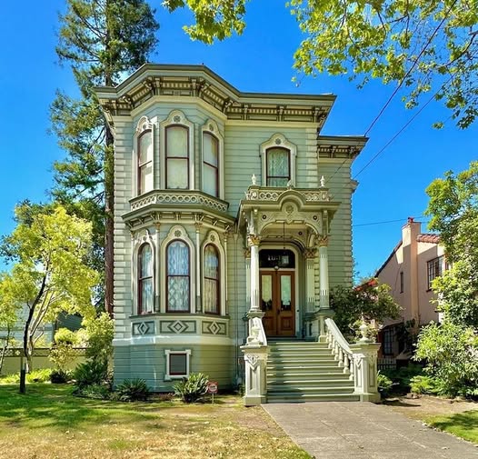 Ornate Victorian house exterior with stairs, bay windows, and trees on a sunny day