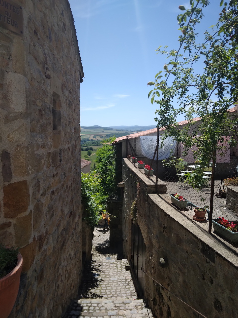 Narrow stone alley between old walls with mountain vista and potted plants