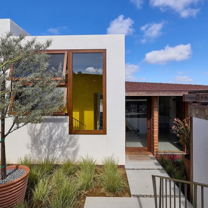 Modern house exterior with large windows, brick walls, and landscaped garden under a blue sky