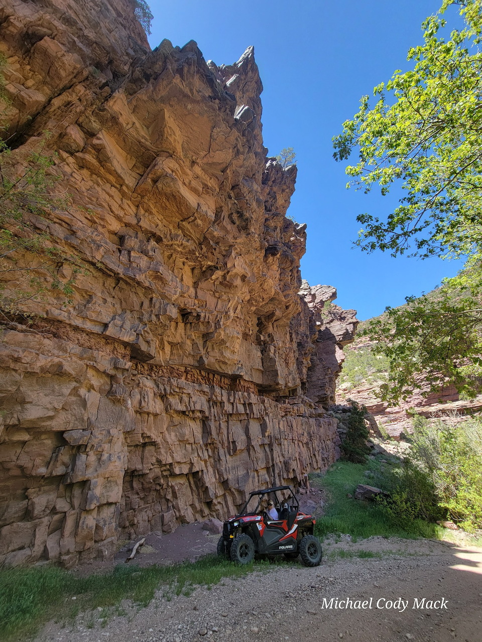 Rocky canyon wall with a parked ATV, trees, and blue sky above