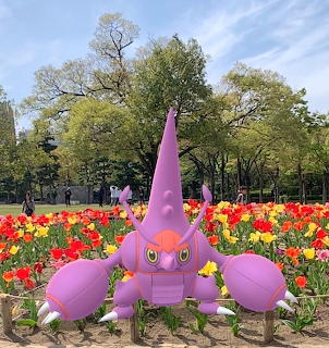 Pink Pokémon figure surrounded by colorful tulips in a park garden