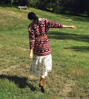 Woman in burgundy patterned top and white lace skirt standing on green lawn