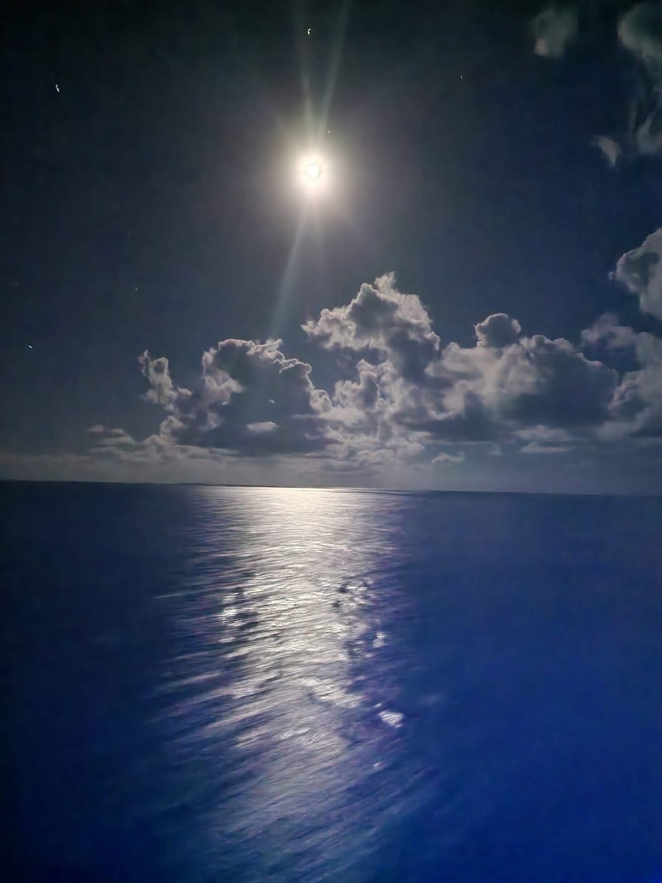 Full moon reflecting on calm ocean at night with clouds on the horizon