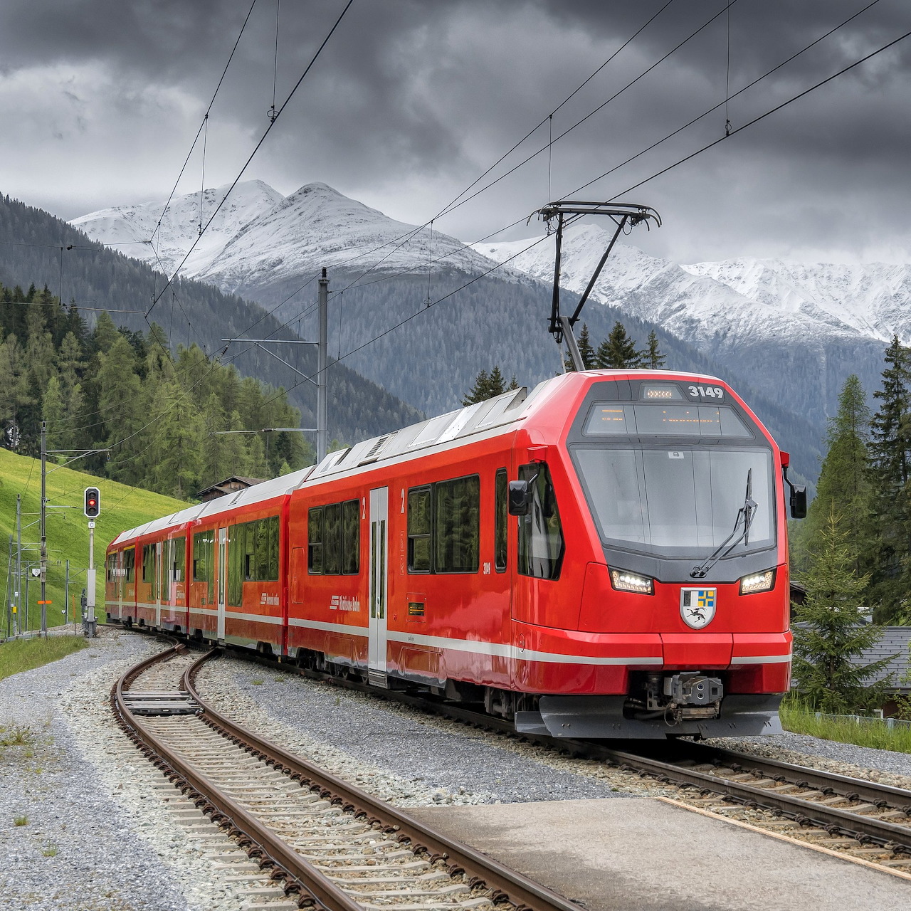 Red passenger train on a curved railway track with snowy mountains behind