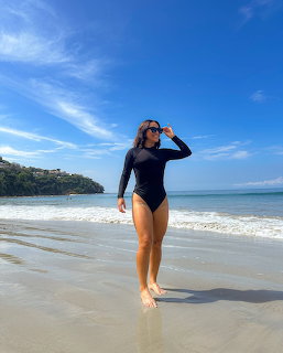 Woman in black swimsuit standing in shallow beach water on sunny day