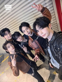 Five young men taking a group selfie indoors near a metal shutter wall