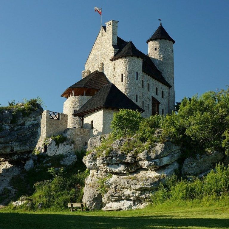 Medieval stone castle on a rocky hillside with trees under a clear blue sky