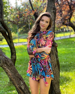 Young woman in colorful tropical print dress leaning against a tree in a green park