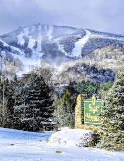 Snowy ski slopes on Sugar Mountain above evergreen trees and a resort sign