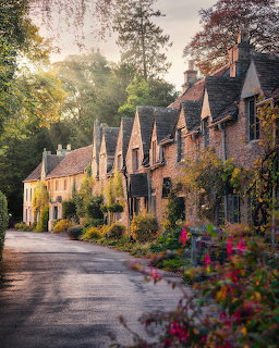 Row of historic stone cottages with gabled roofs along a village road with flowering gardens in the Cotswolds