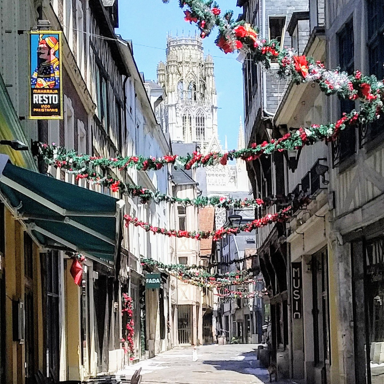Narrow decorated street in Rouen with garlands and a cathedral tower in the distance