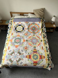 Handmade quilt with colorful hexagonal floral patterns on white fabric draped over bed