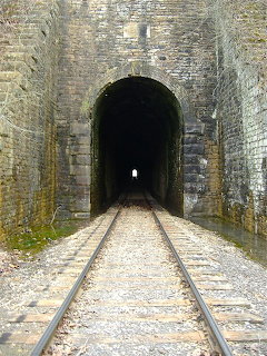 Stone railway tunnel entrance with tracks disappearing into darkness and a faint light at the far end
