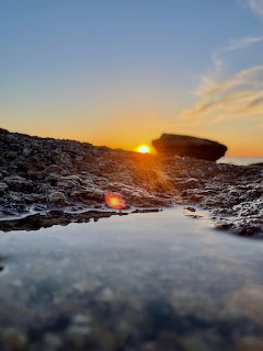 Sunset over rocky shoreline with sun reflecting in a still tidal pool among dark rocks