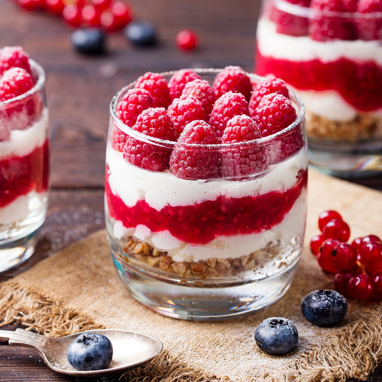 Layered berry parfait desserts with raspberries, cream, and fruit compote in clear glasses