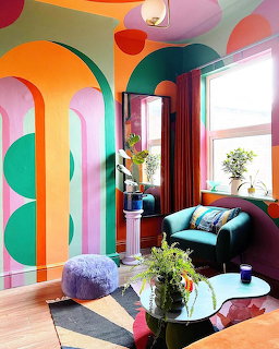 Bright living room with colorful geometric wall art, teal curved sofa, and large arched windows