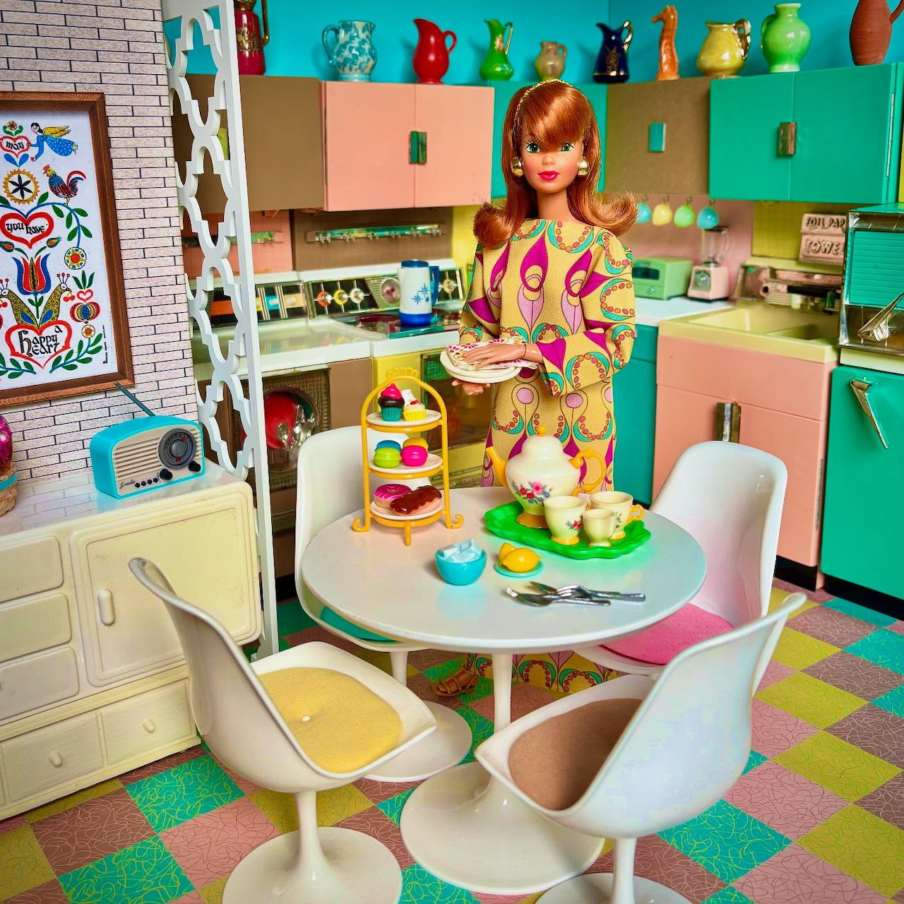 Red-haired doll in a colorful retro kitchen with a round table and white chairs