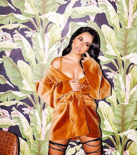 Woman in orange velvet robe posing in front of tropical banana leaf wallpaper