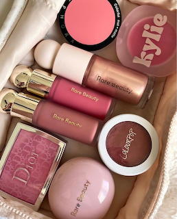 Pink makeup products arranged on white background including blush, lipsticks, and Dior compact
