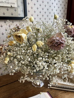 Dried flower bouquet with baby's breath and faded roses in a glass vase on a wooden desk