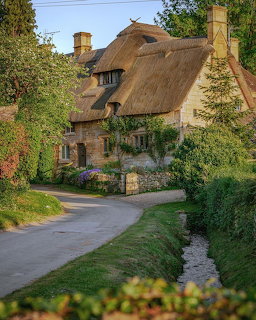 Traditional English thatched roof cottage with brick walls and flowering garden on a country road