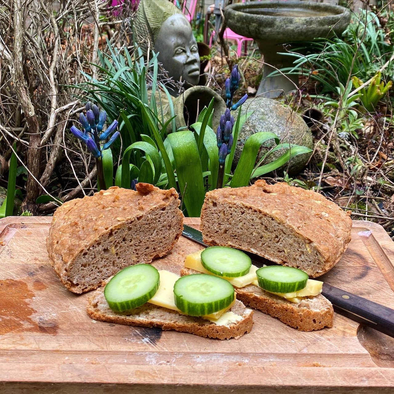 Sliced whole grain bread with cucumber on wooden cutting board outdoors