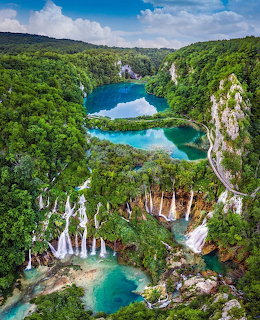 Aerial view of turquoise lakes connected by waterfalls surrounded by dense green forest